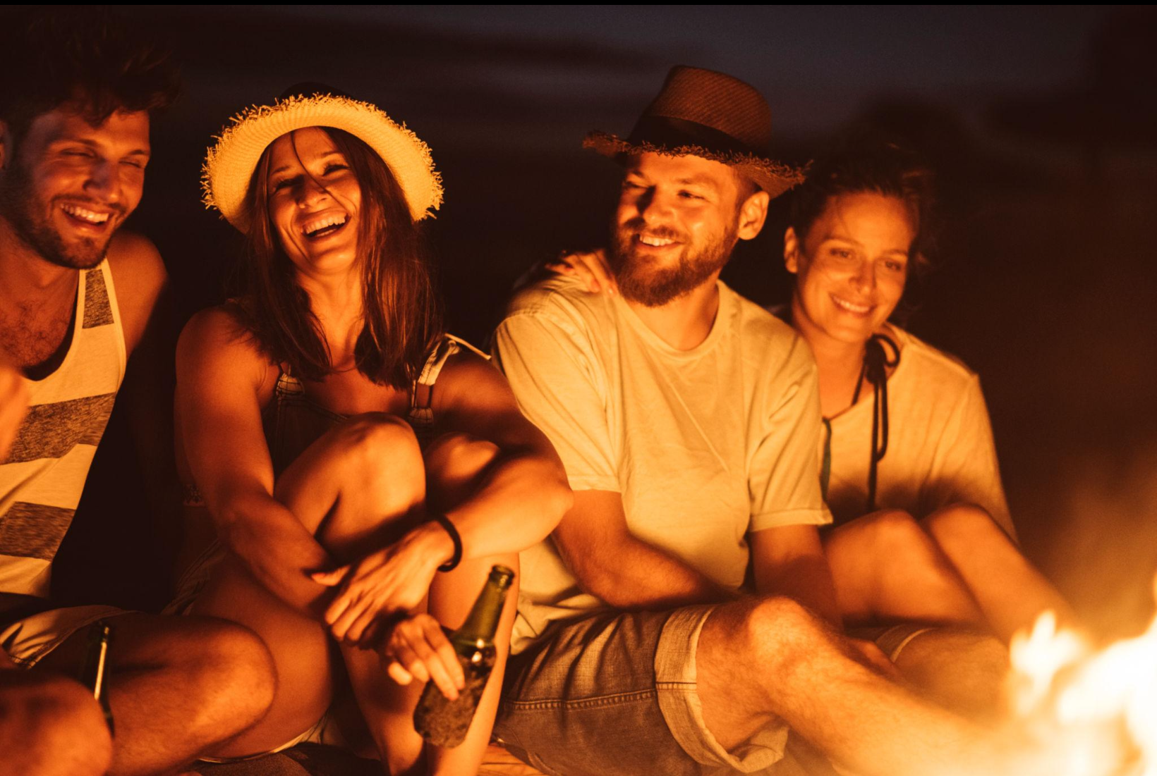 Friends laughing together by a bonfire on the beach